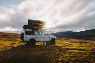 White Land Rover Defender with roof tent camping on a Scottish mountain